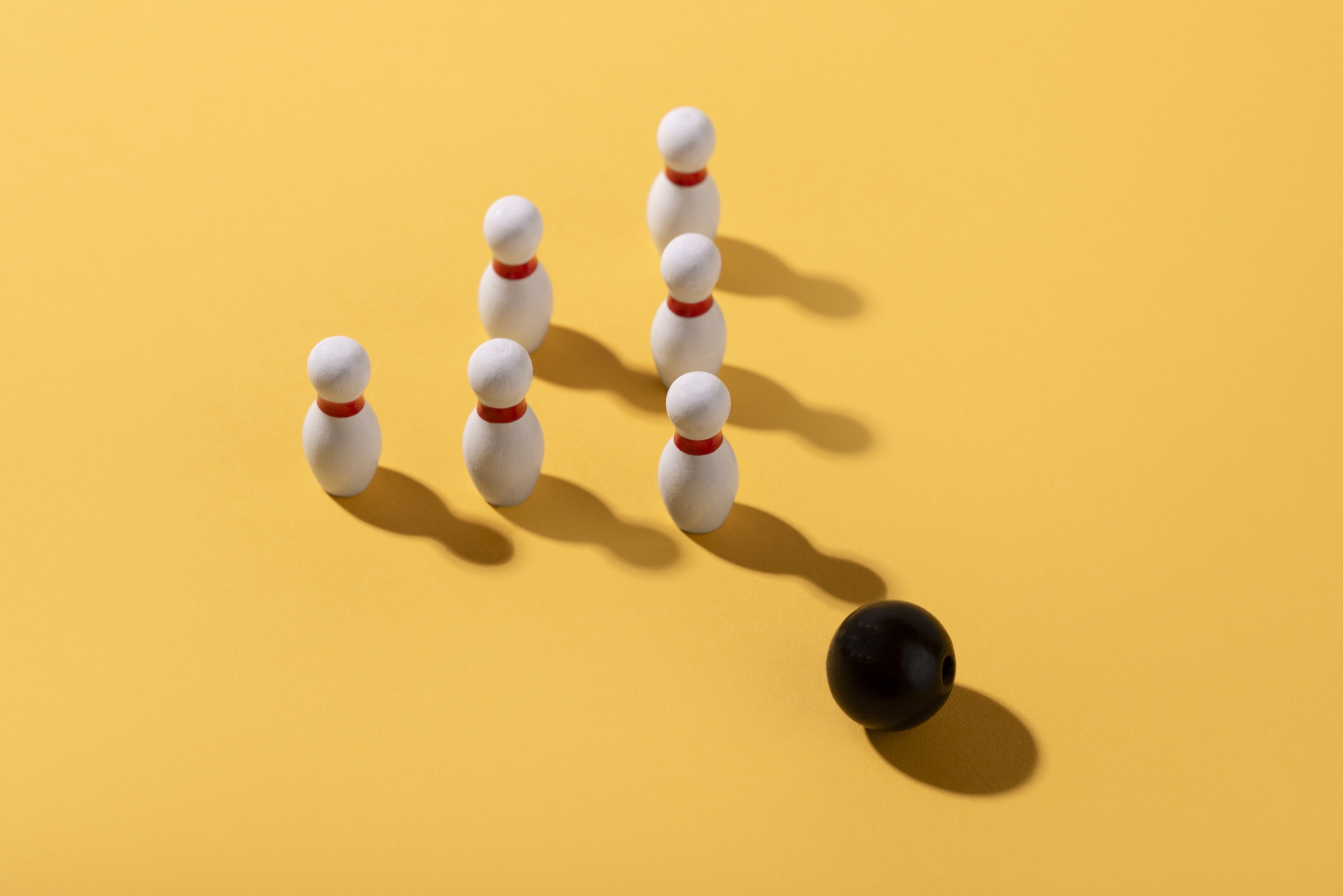 A black ball lined up with white bowling pins on a yellow surface